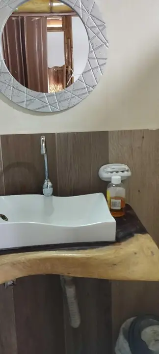 Baño con espejo redondo y lavabo sobre una tabla de madera natural