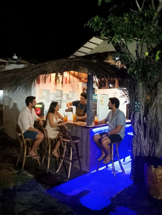 Huéspedes conversando de noche en la barra iluminada de la cafetería bar bajo techo de paja