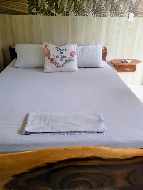 Cama doble con cabecera de madera natural, almohada en forma de corazón y toalla doblada