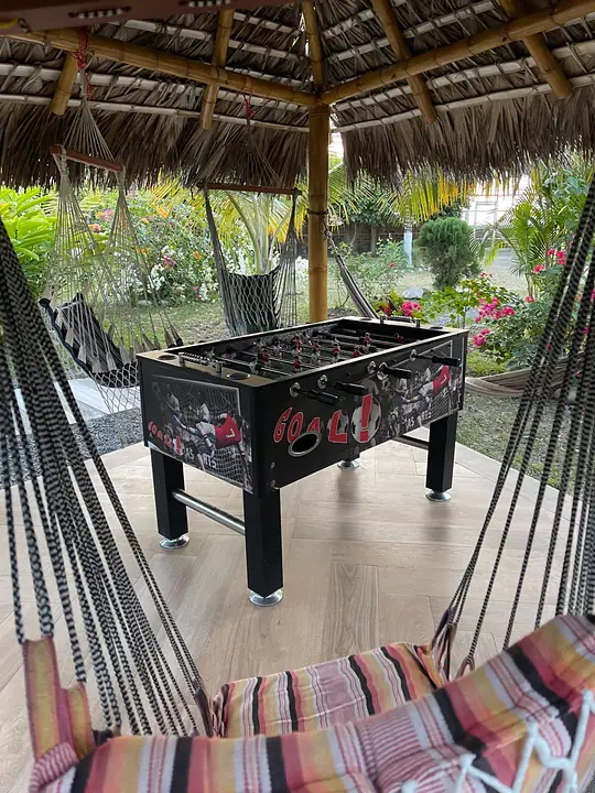 Hamacas de colores y una mesa de futbolín bajo un techo de paja