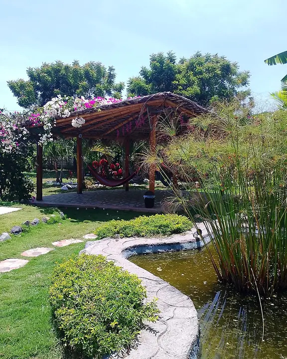 Jardín con camino de piedra, estanque y una glorieta de madera con flores
