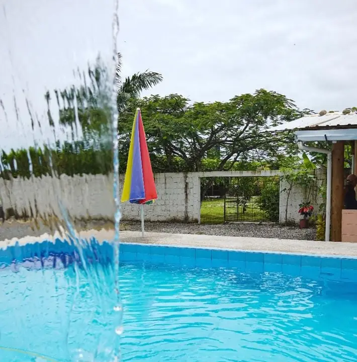 Chorro de agua cayendo en cascada sobre la piscina, con una sombrilla de colores al fondo