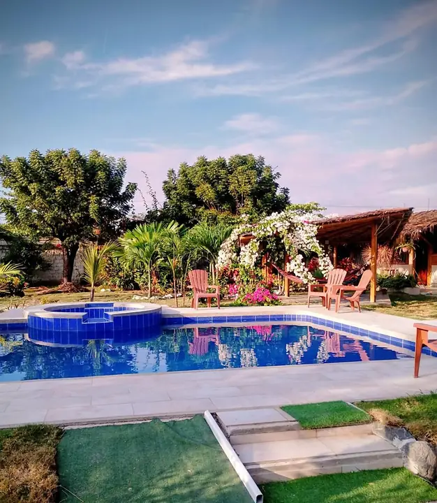 Piscina al aire libre rodeada de jardines, palmeras y cabañas bajo el cielo azul
